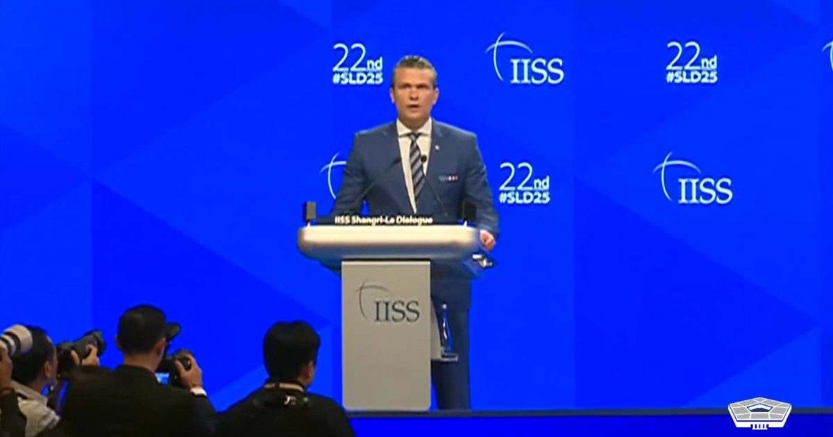 Speaker addressing the audience at the 22nd IISS Shangri-La Dialogue conference, with photographers capturing the moment against a blue backdrop.