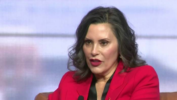 Governor speaking during a panel discussion, wearing a red blazer and addressing the audience with a serious expression.
